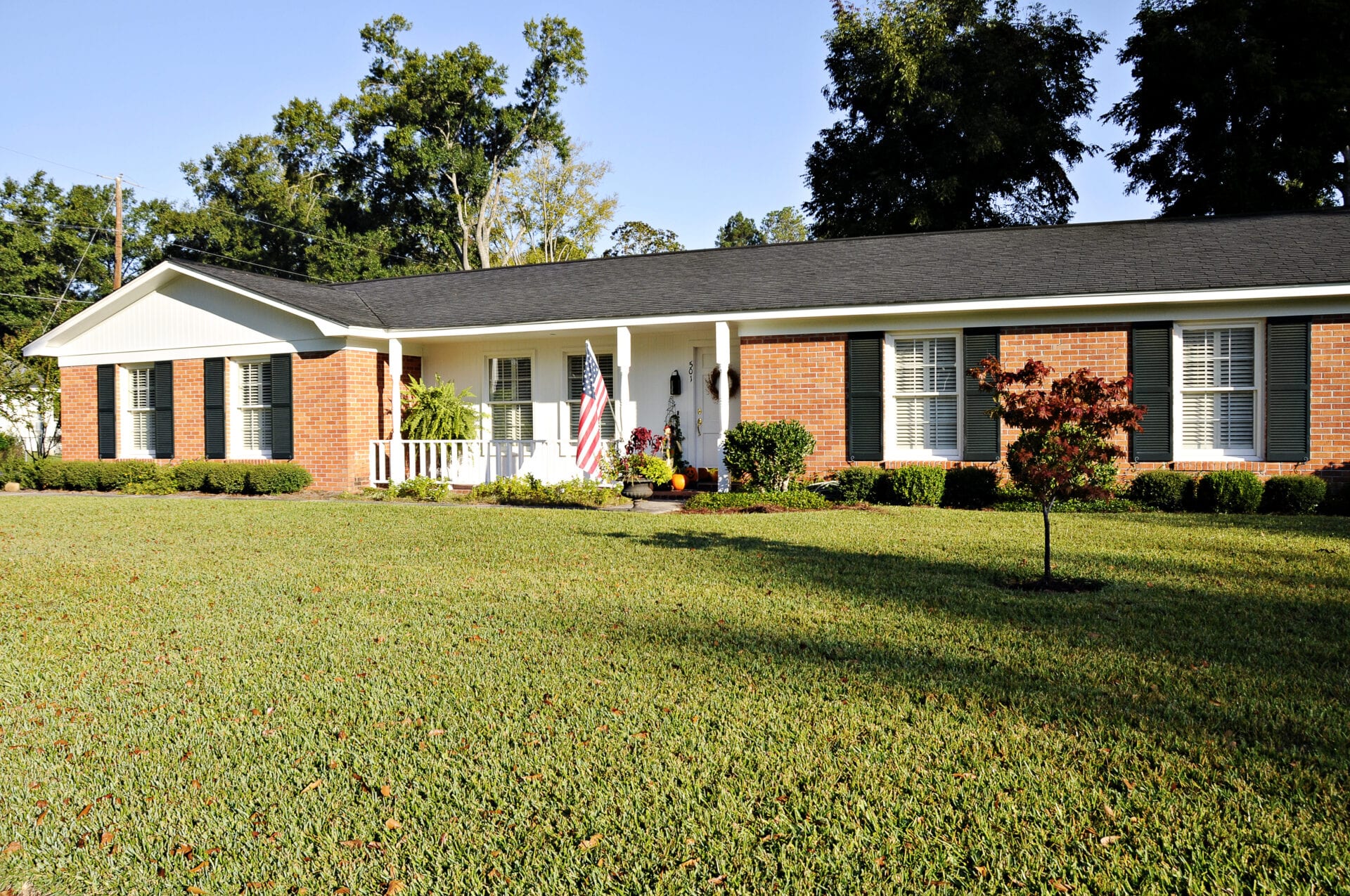 Lovely Ranch style home of red brick, white trim and black shutters with an American Flag.